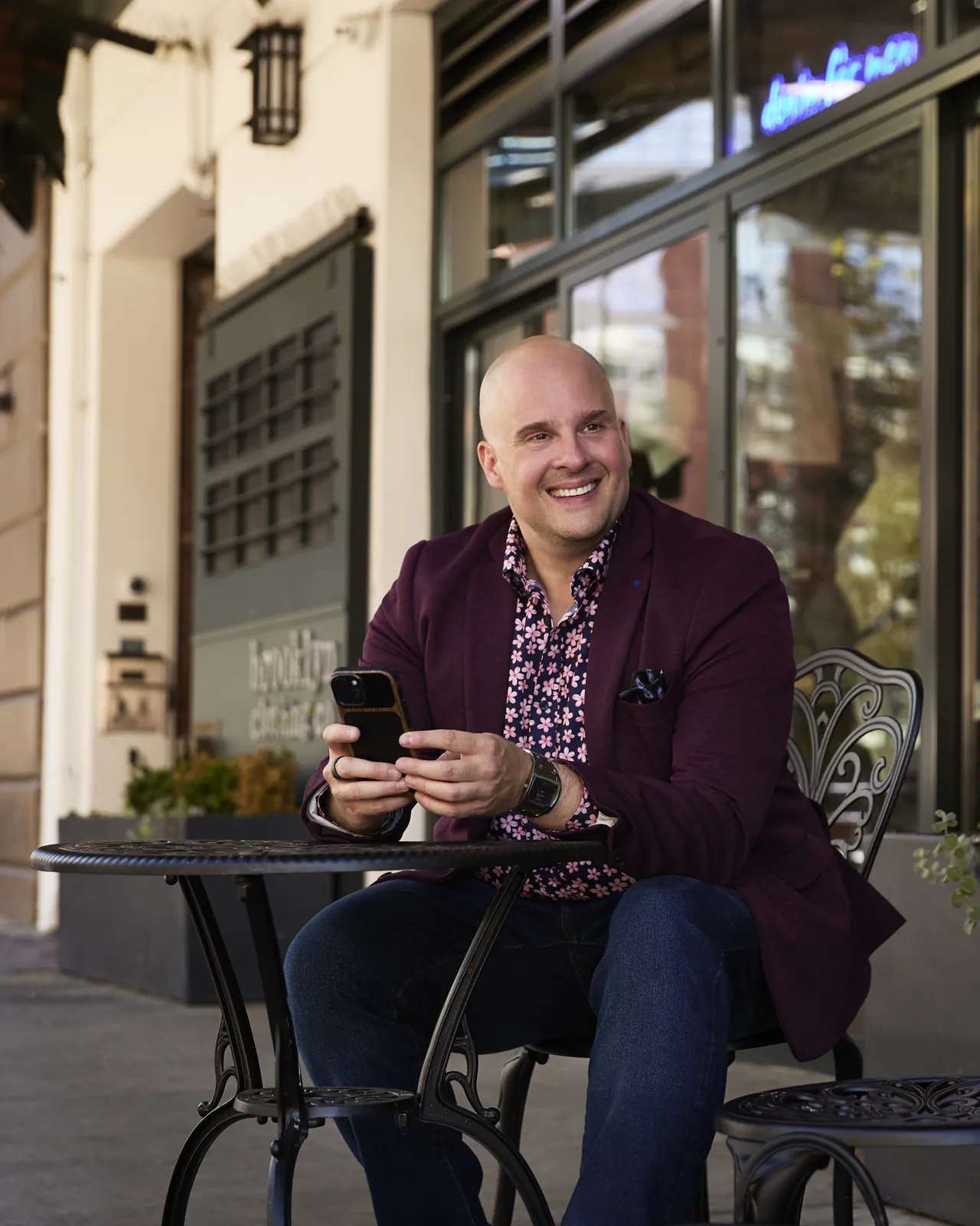 Dr. Stephen de Wit in a plum jacket, smiling, seated outside a café